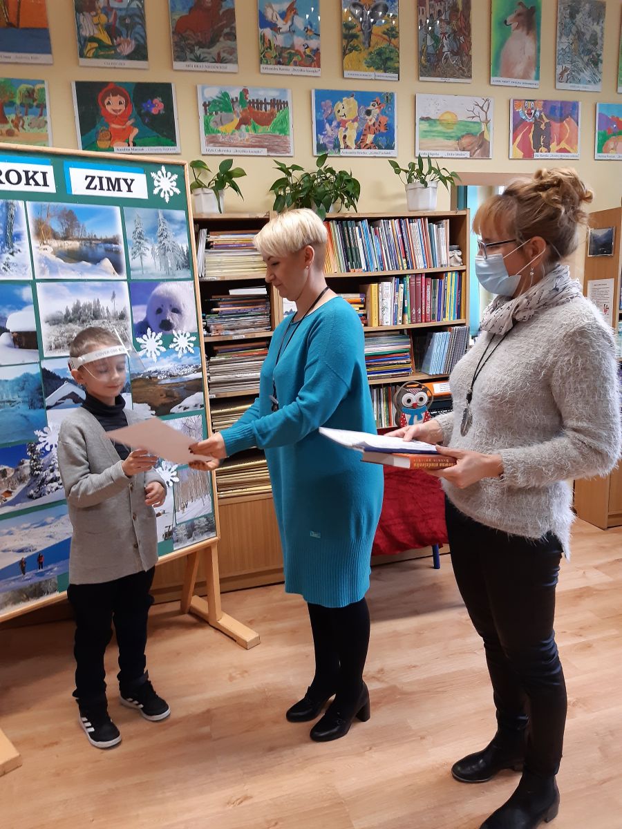 Powiększ zdjęcie. Wicedyrektor  w bibliotece szkolnej wręcza uczniowi dyplom. 