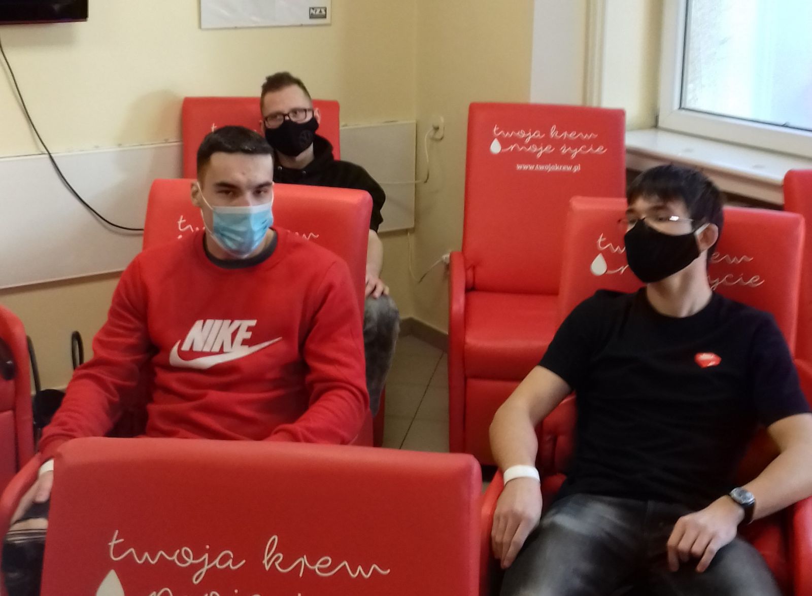Trzech chłopaków w amseczkach na twarzy siedzi na czerwonych fotelach