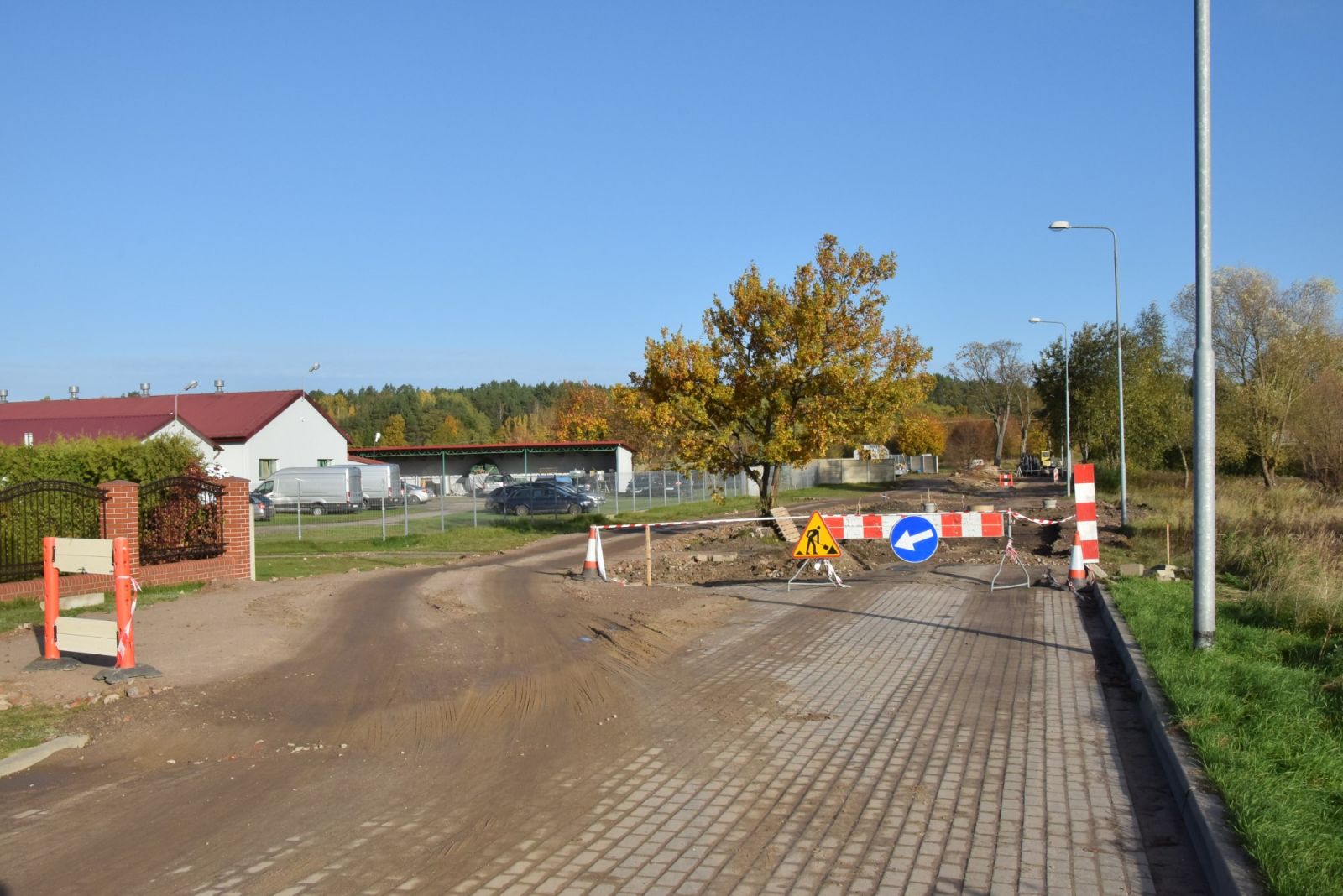 Zamknięta droga, znaki ostrzegawcze, drzewa, lampy, niebieskie niebo, budynek