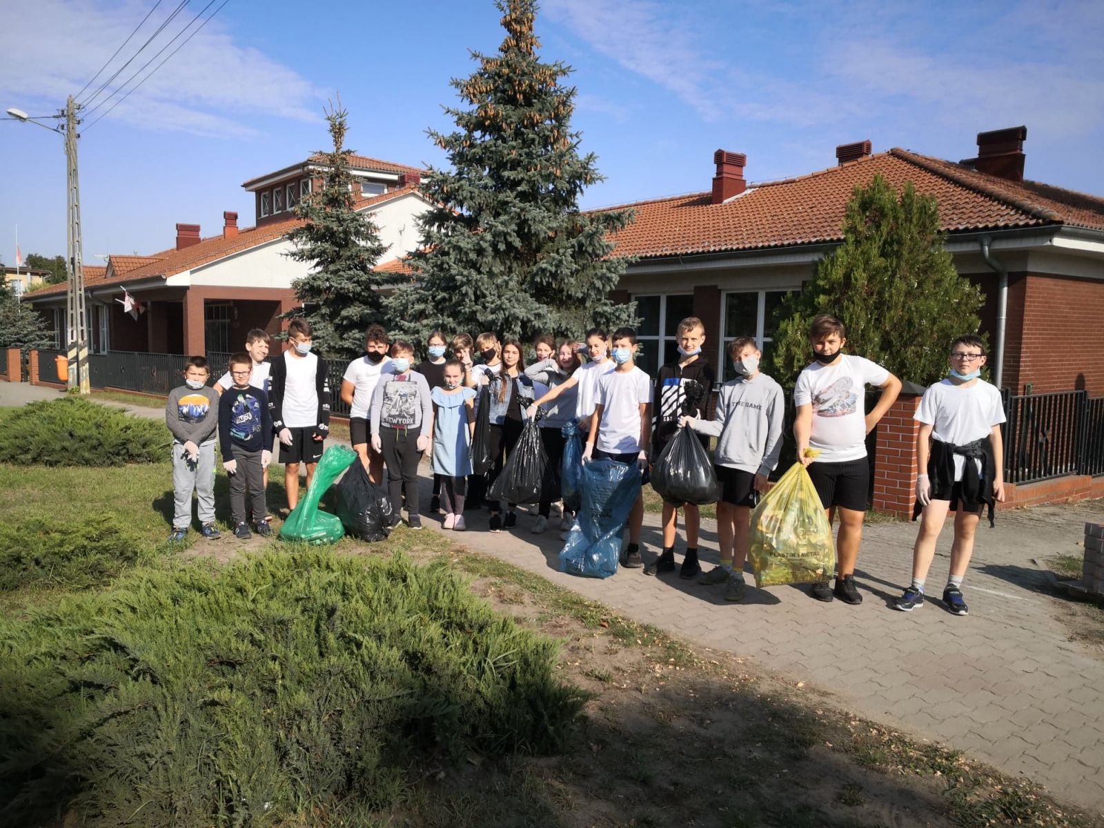 Grupa uczniów z workami, w tle budynek szkoły w Cychrach, niebo, zieleń