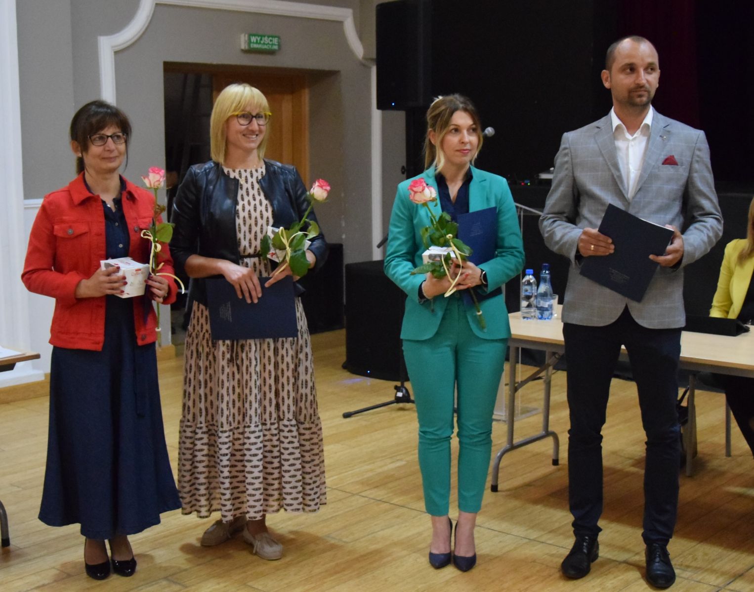 Powiększ zdjęcie. na sali stoją trzy kobiety z różą w ręku i mężczyzna