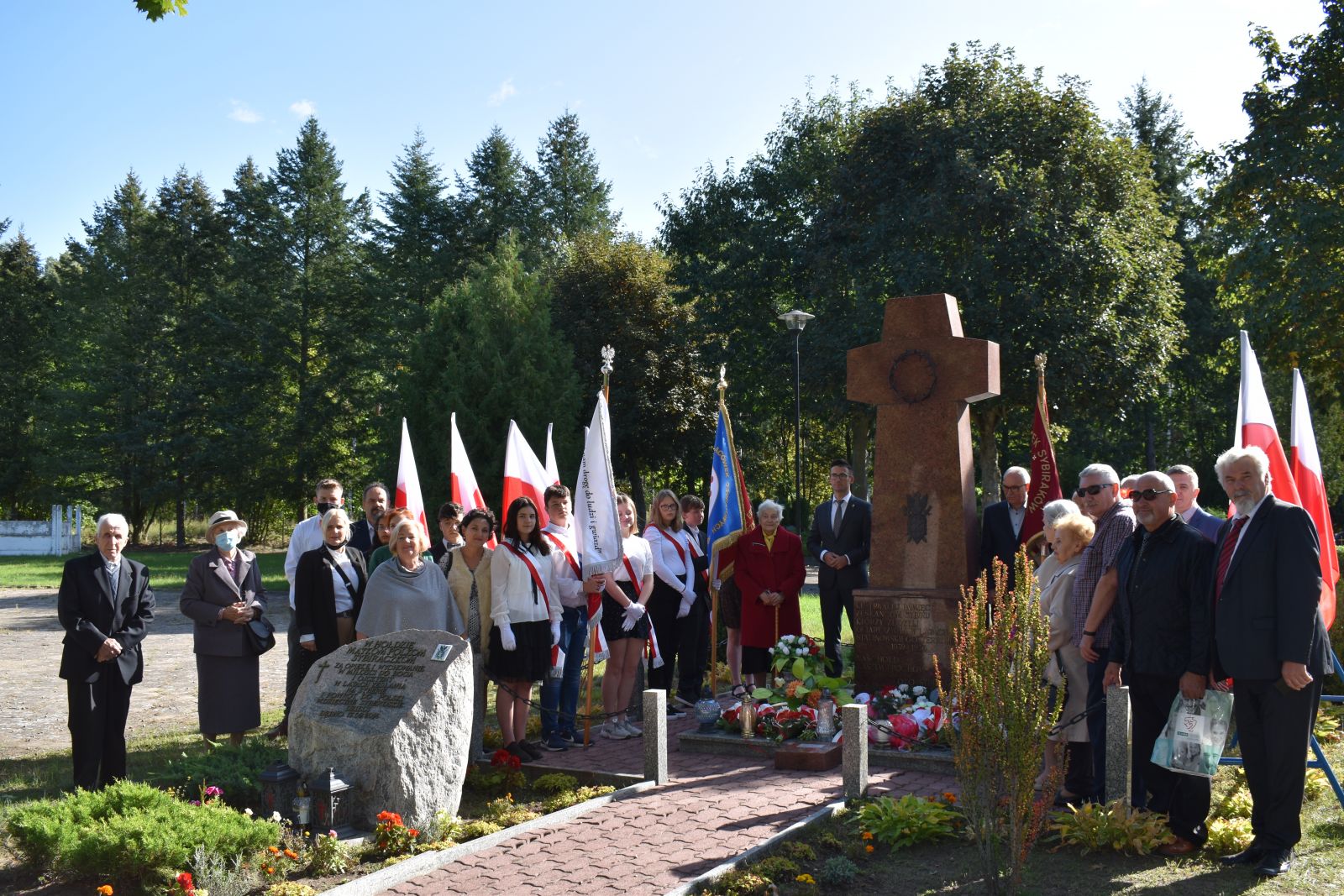 Zgromadzeni goście przed Pomnikiem Sybiraków. Niebo, drzewa