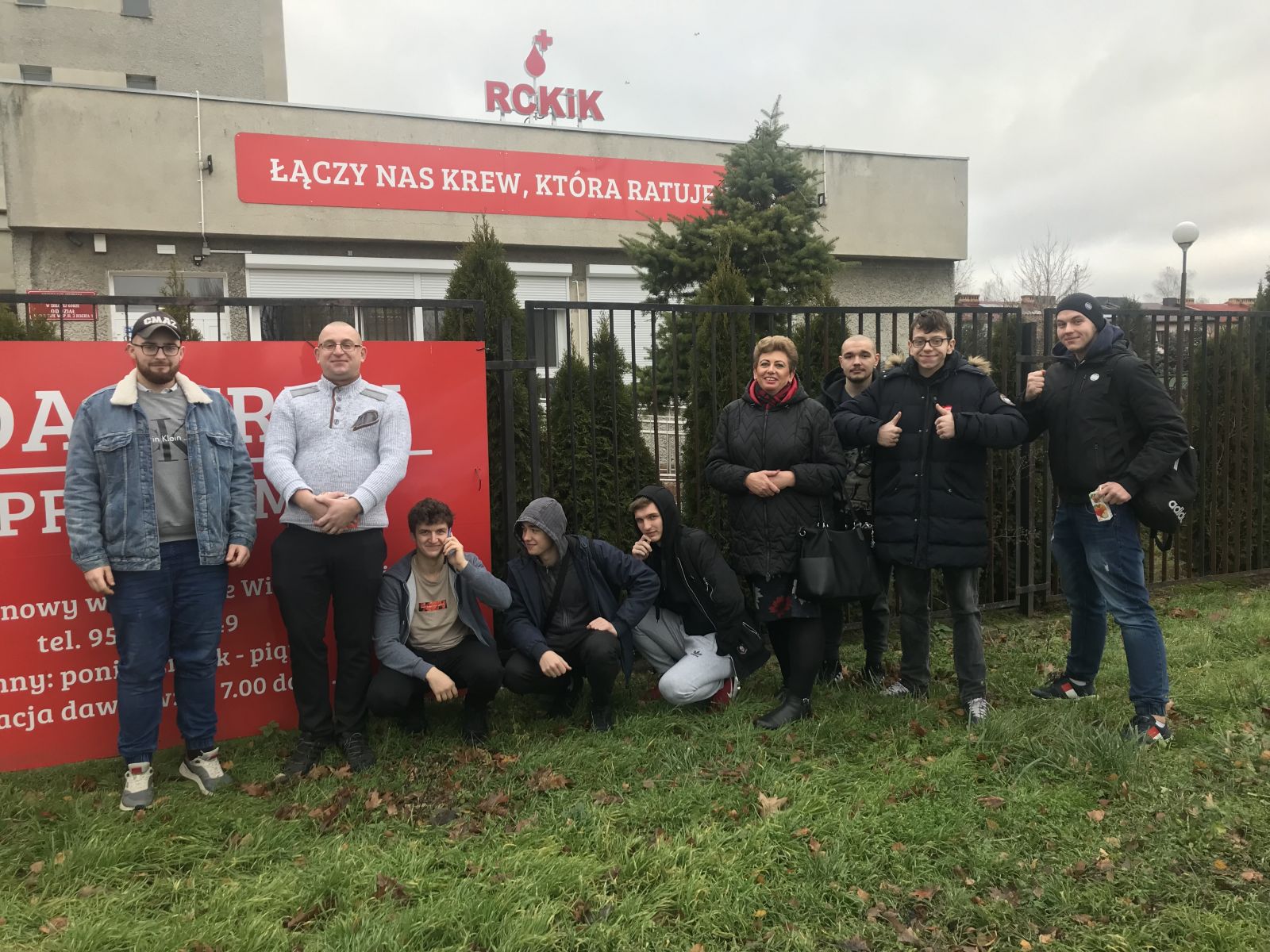 Powiększ zdjęcie. Grupa młodzieży stoi przed punktem krwiodawstwa