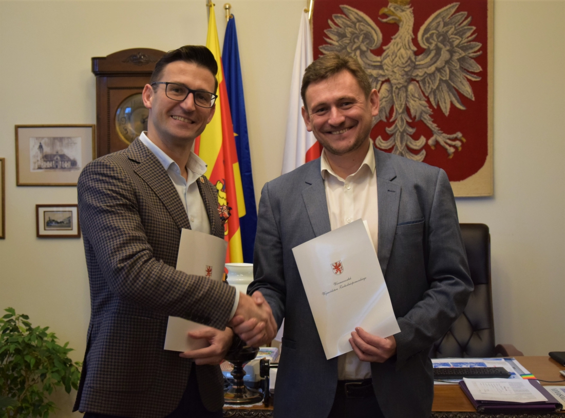 Powiększ zdjęcie. Burmistrz Dębna i wicemarszałek ściskają sobie dłoń, trzymają dokumenty w dłoni