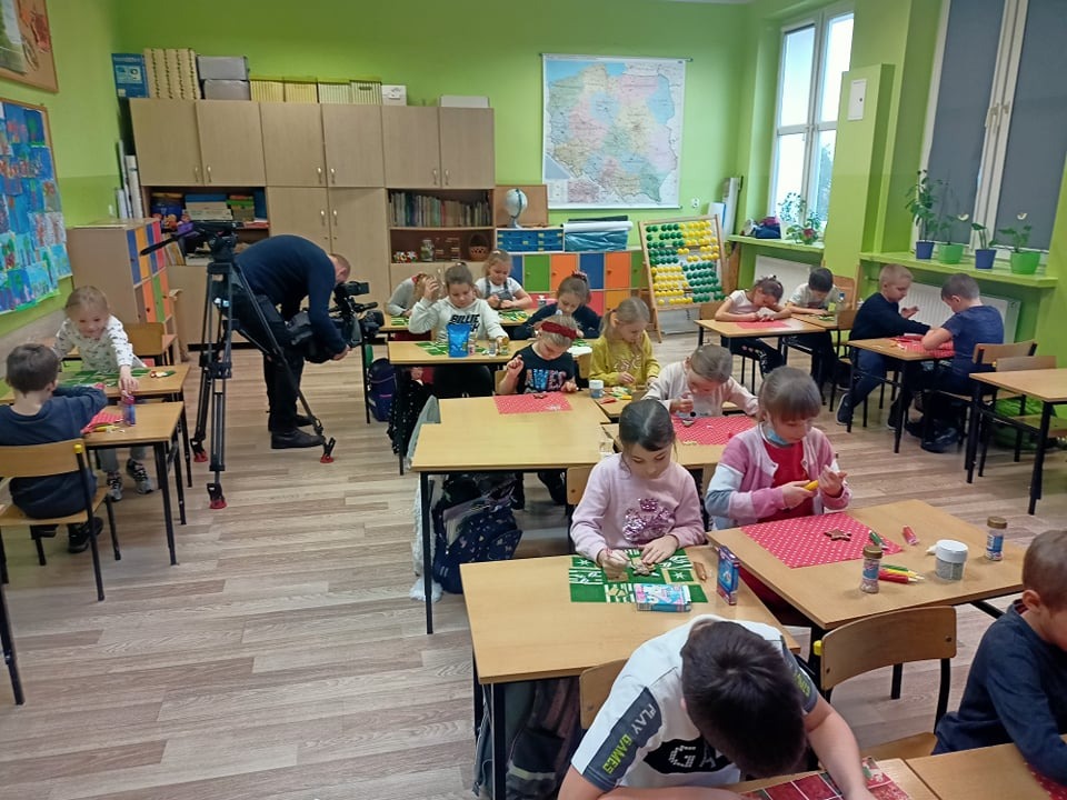 Powiększ zdjęcie. Telewizja realziuje materiał w klasie uczniwie wykonują prace dla żołnierzy
