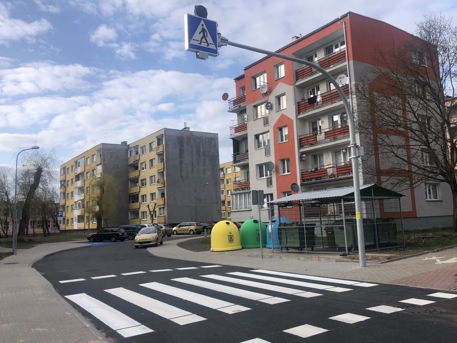 Niebo, znak na wysięgniku nad jezdnią, bloki mieszkalne, drzewa