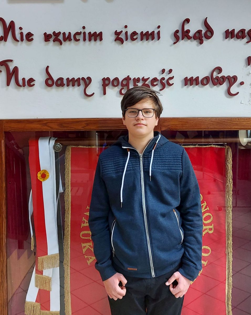 Powiększ zdjęcie. Uczeń Kornel stoi, w tle sztandary w gablocie 