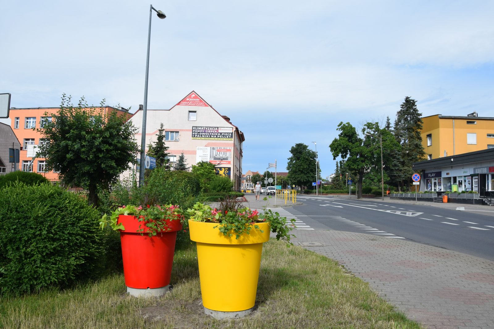 Żółta i czerwona donica z nasadzeniami, na skrzyżowaniu ulic, niebo, krzewy