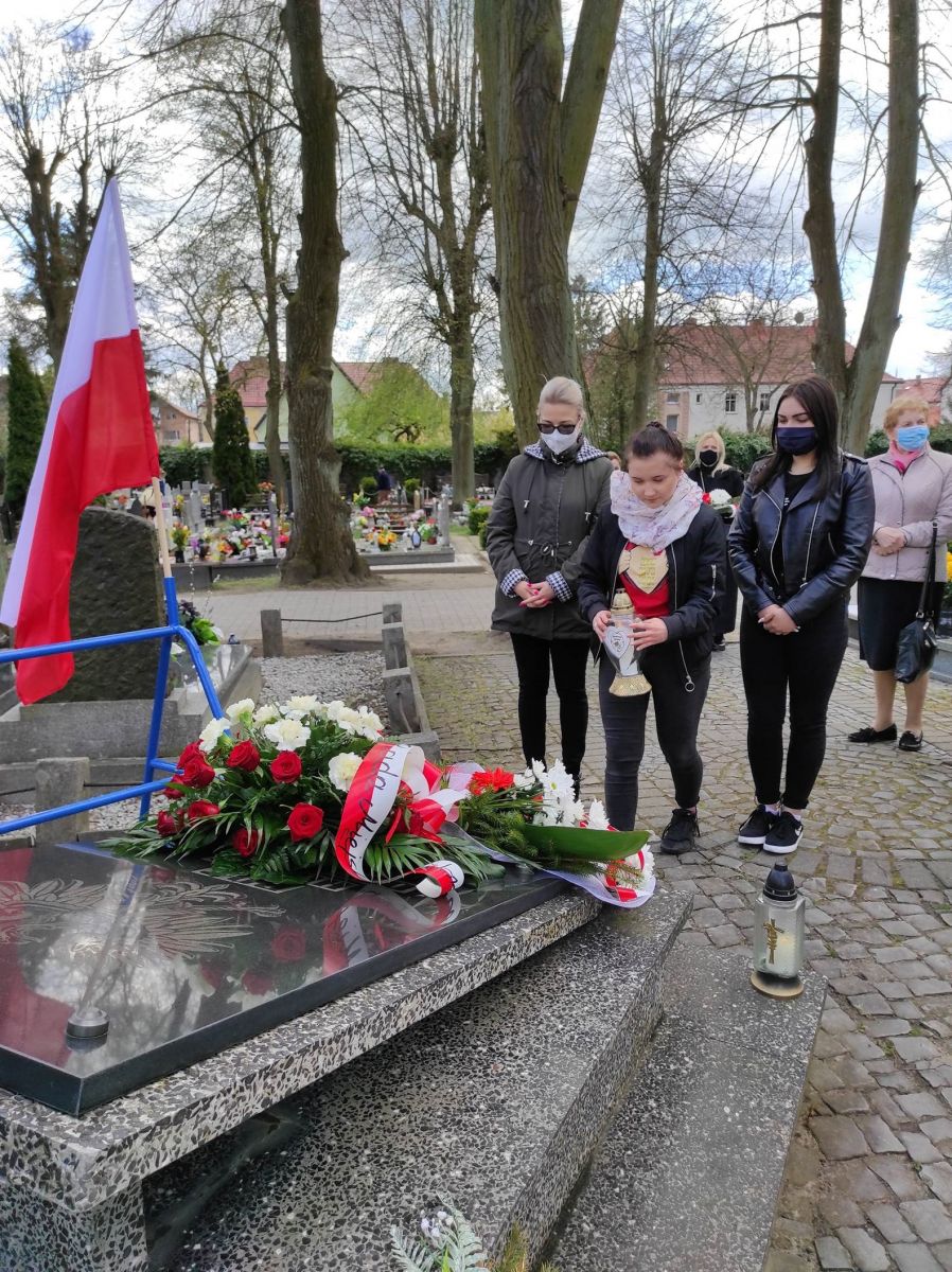 Powiększ zdjęcie. Ludzie składają kwiaty i znicze pod pomnikiem 