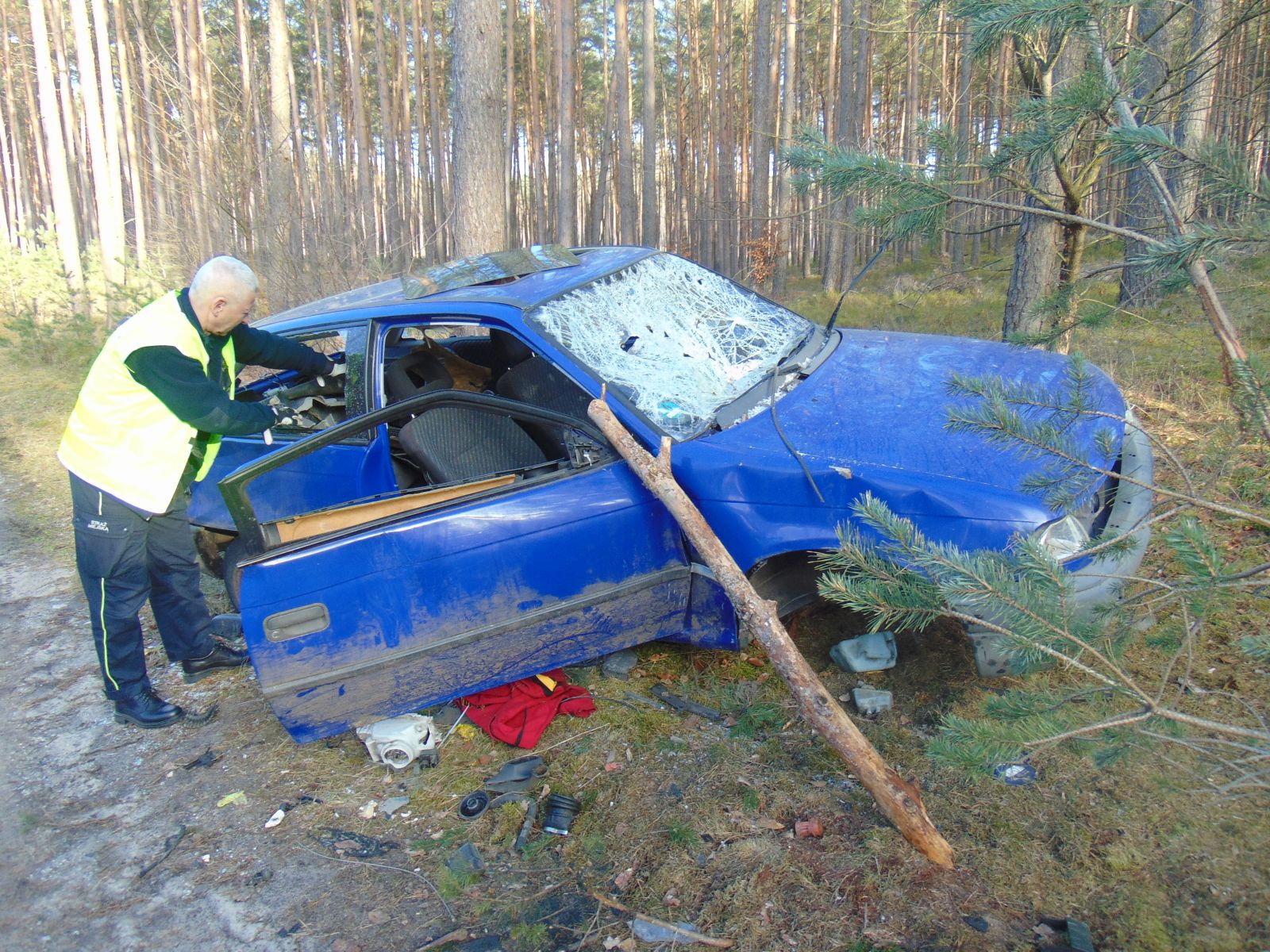 Powiększ zdjęcie. Strażnik zagląda do porzuconego samochodu w lesie