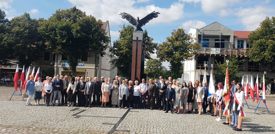 Powiększ zdjęcie. Grupowe zdjecie uczestników na placu, w tle pomnik 