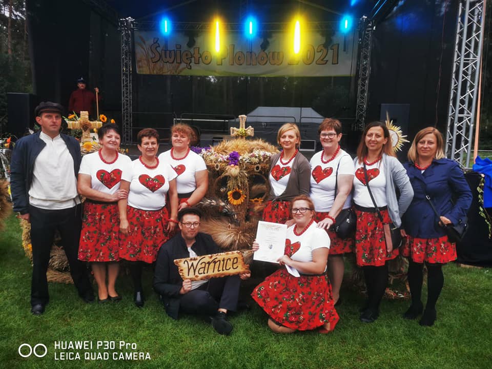 Powiększ zdjęcie. Grupa mieszkańców Warnice, w tle wieniec, scena, zielona trawa