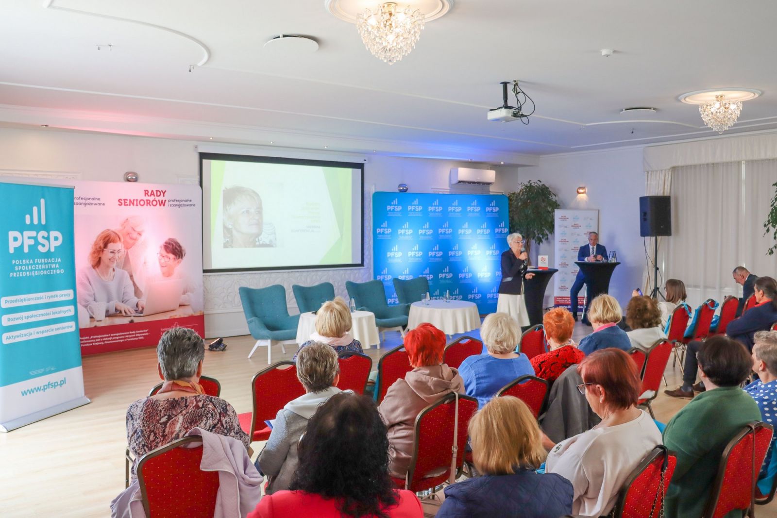 Powiększ zdjęcie. Sala ludzie siedzą, ekran,banery 
