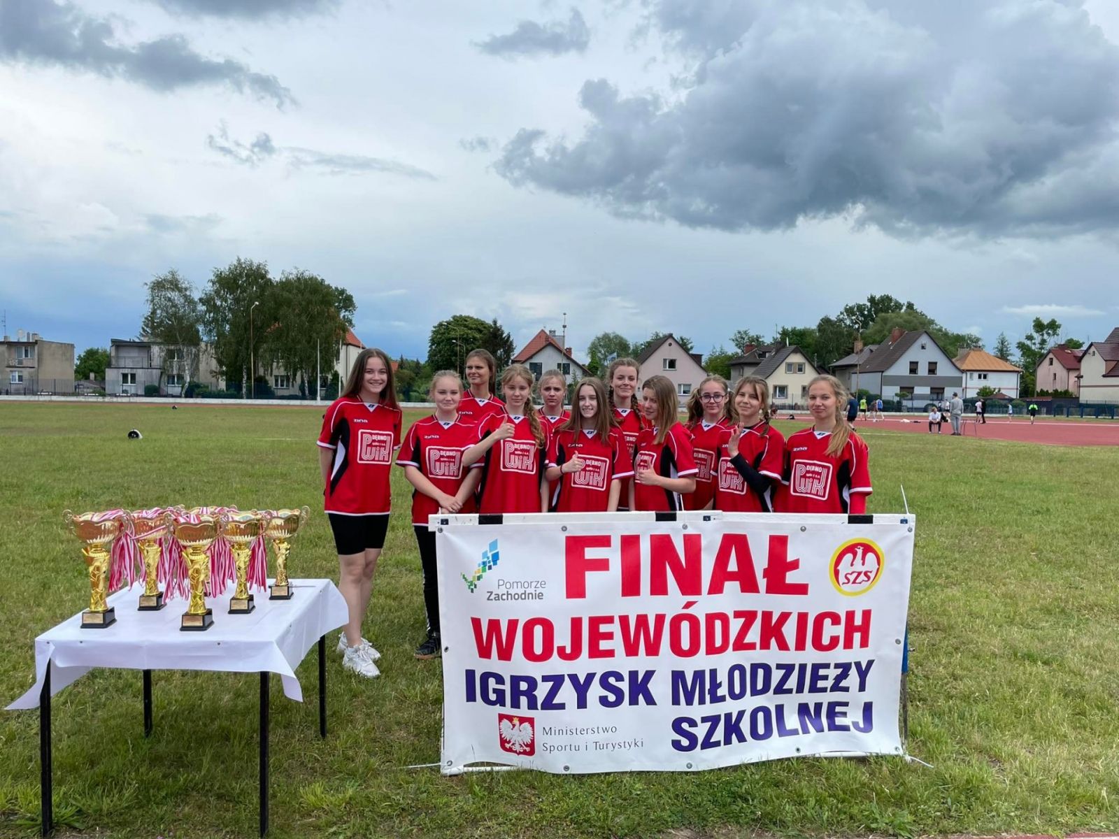 Powiększ zdjęcie. Drużyna dziewcząt w rękach trzyma baner finał wojeówdzkich igrzysk
