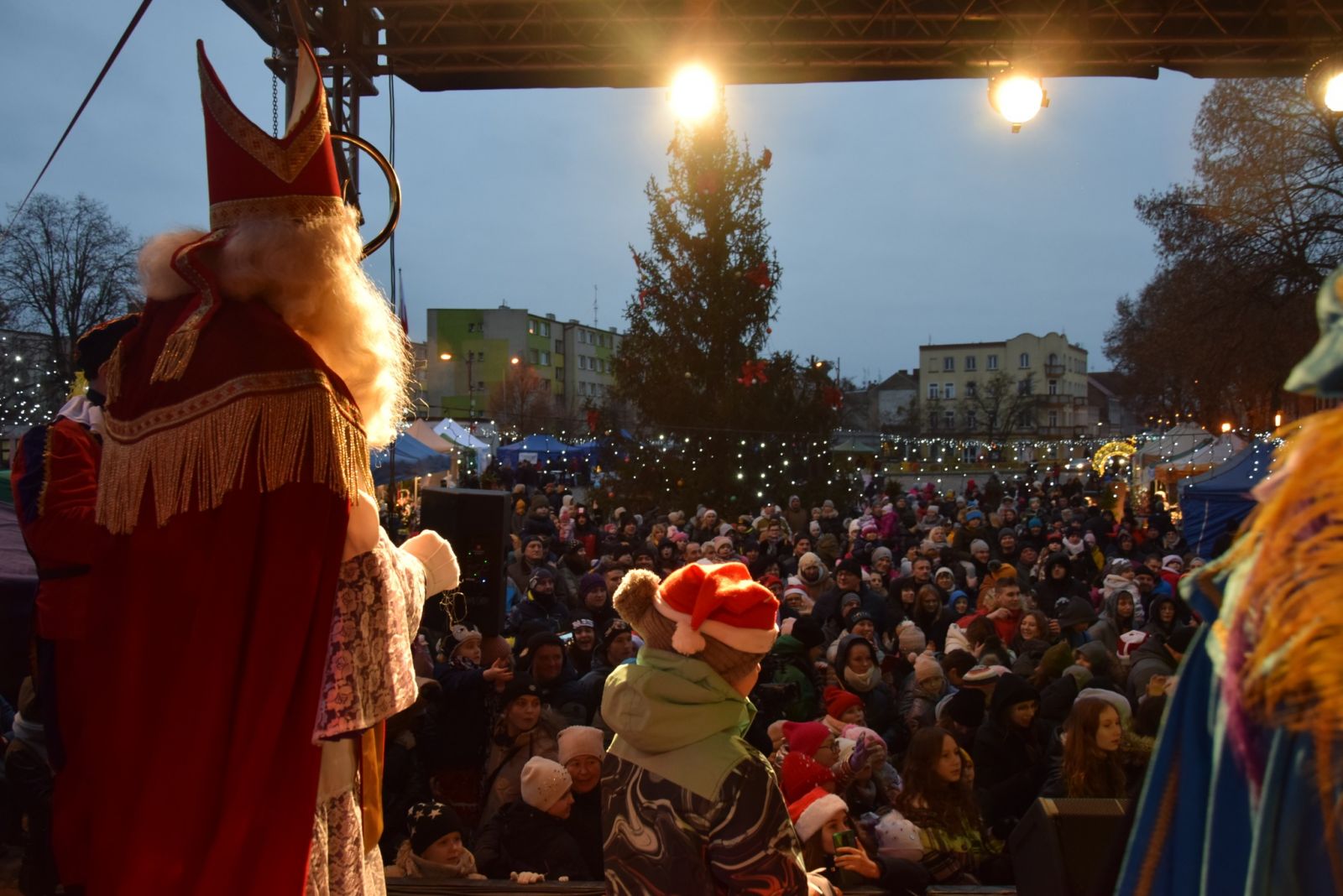 Powiększ zdjęcie. Mikołaj na scenie, w tle tłum dzieci pod ceną 