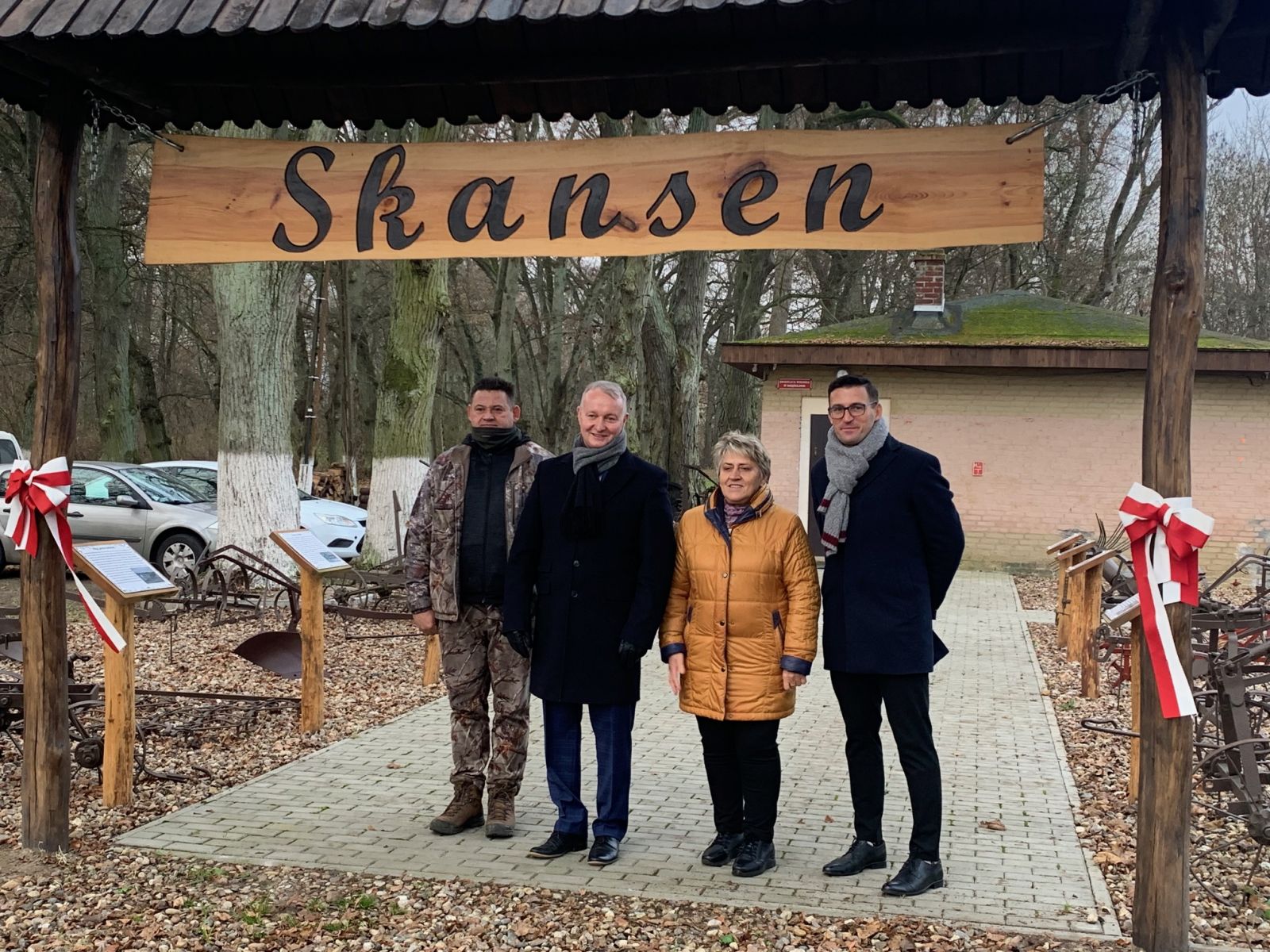 Wicemarszałek, sołtys i burmistrz stoją pod bramą z napisem skansen
