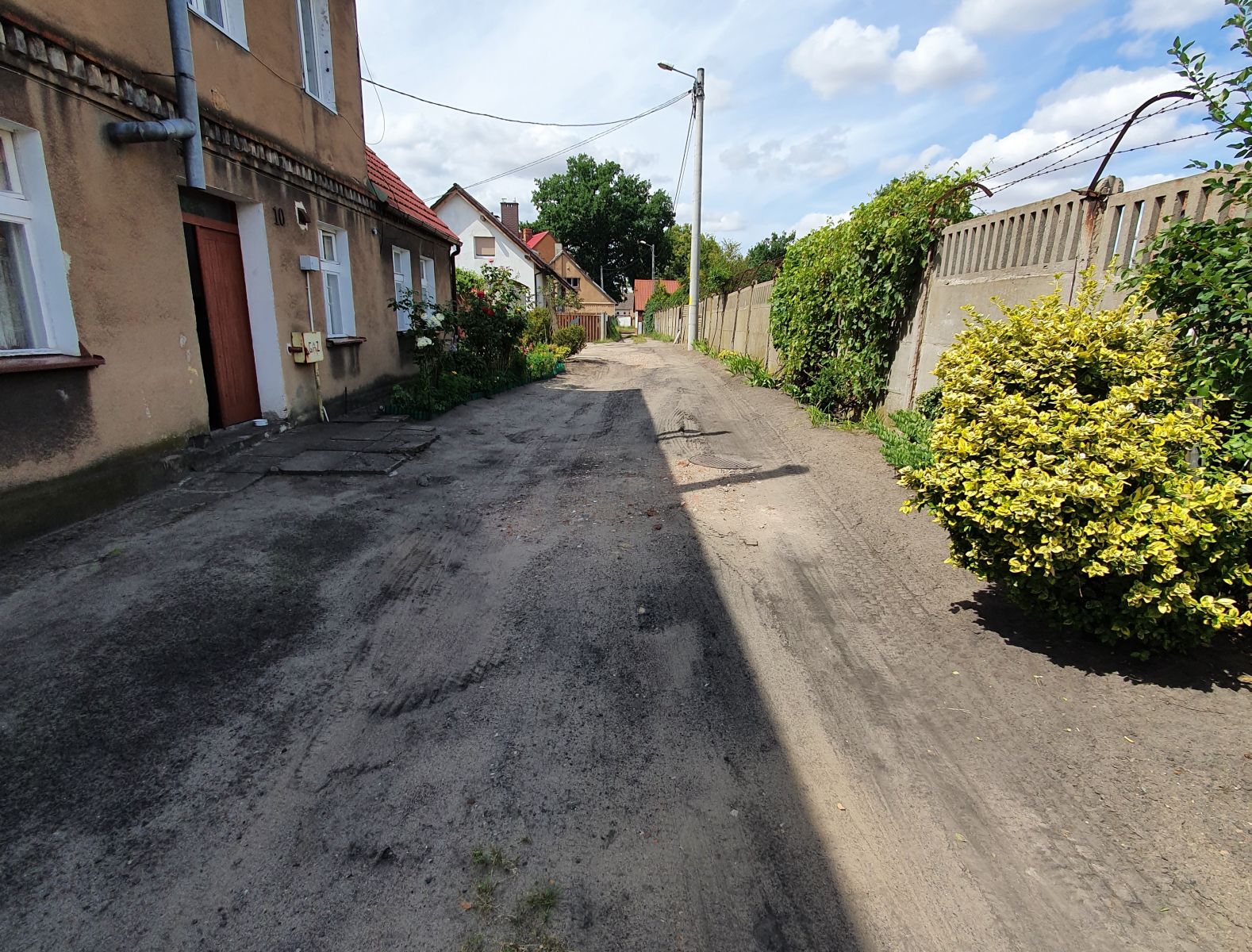 Ulica Zakręt, budynek wielorodzinny, płot betonowy, niebo, krzaki