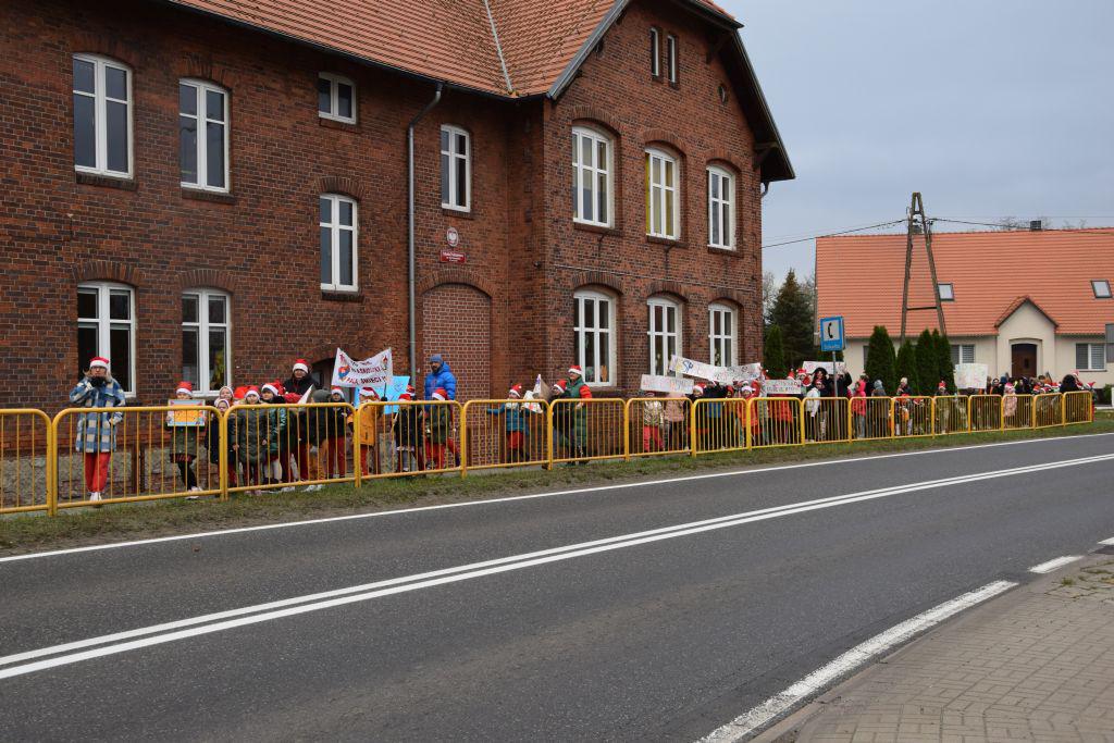 Dzieci idą w rzędzie przed szkołą, przy ruchliwej ulicy, barierki 