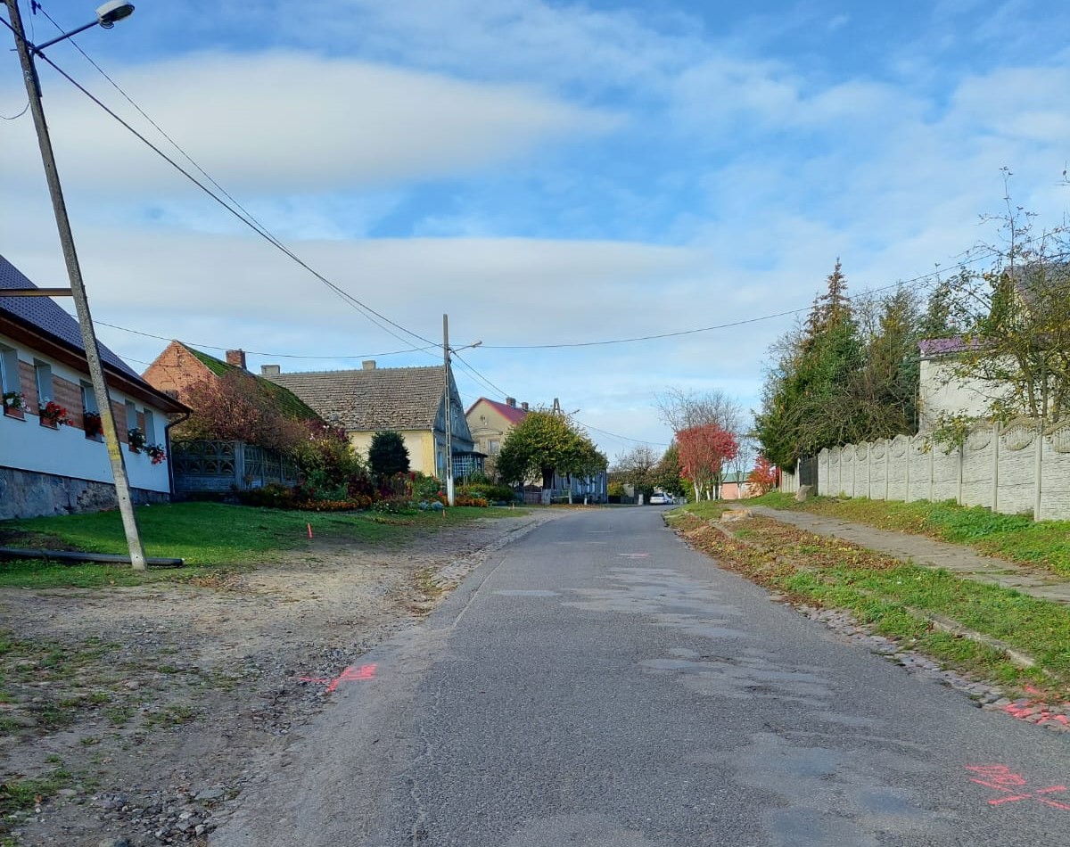 Droga, po obu stronach zabudowania, drzewa, z prawej strony chodnik., pas zieleni