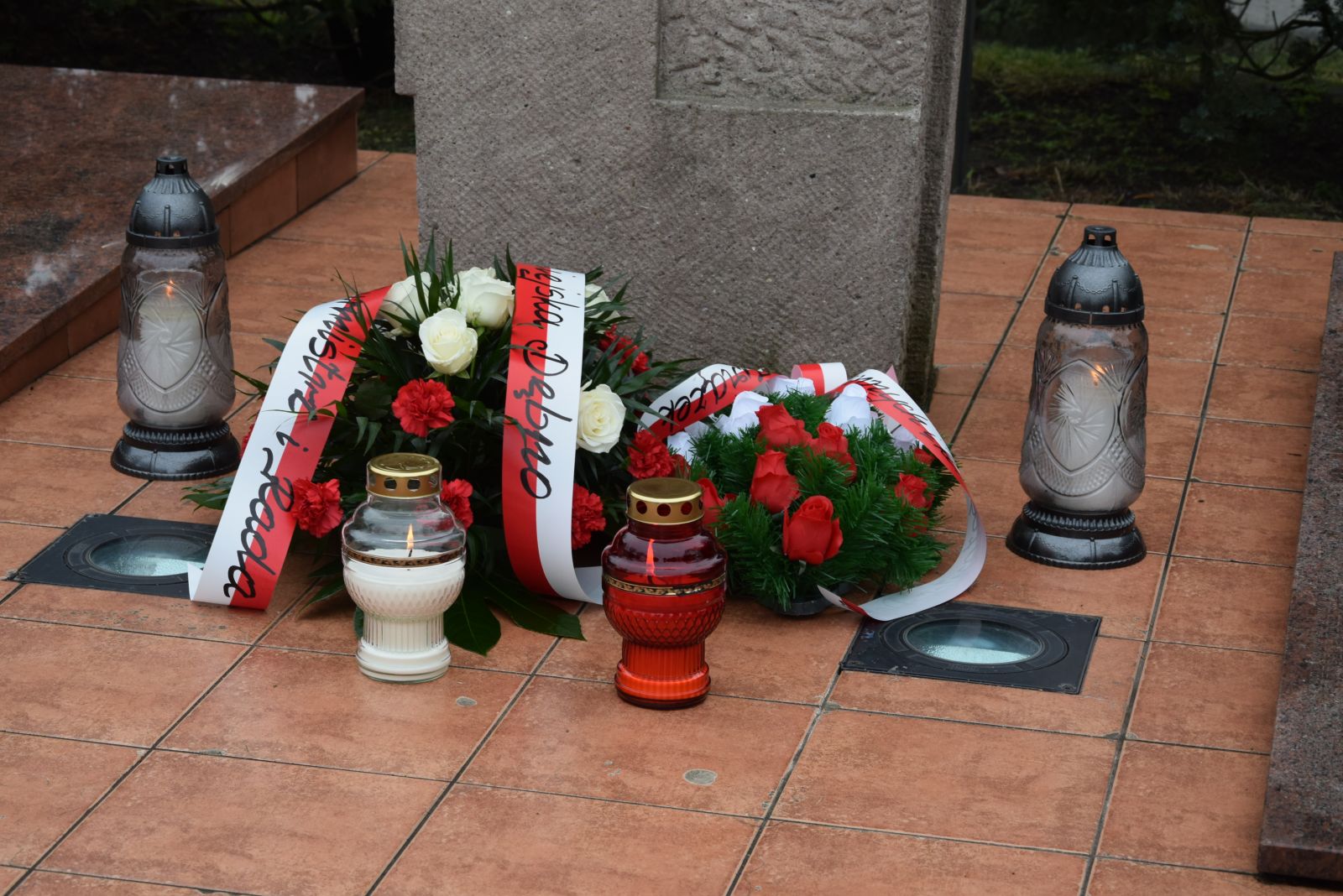 Powiększ zdjęcie. Kwiaty  i znicze na płycie pomnika