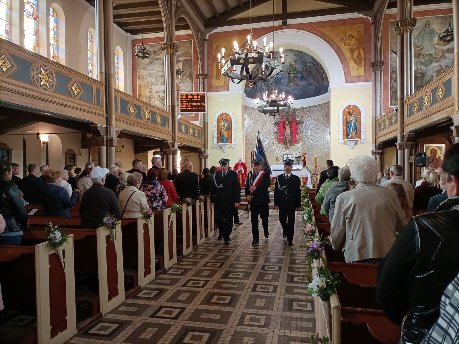Strażacy ze sztandarem idą środkiem kościoła