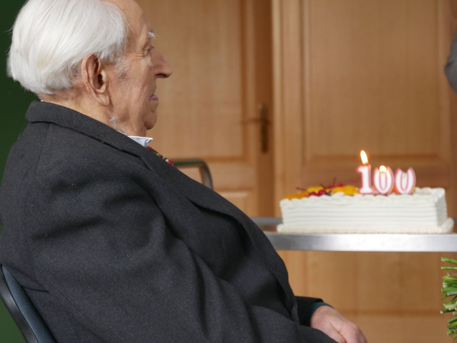 Powiększ zdjęcie. Jan Zaremba siedzi, w tle tort ze świeczkami 100