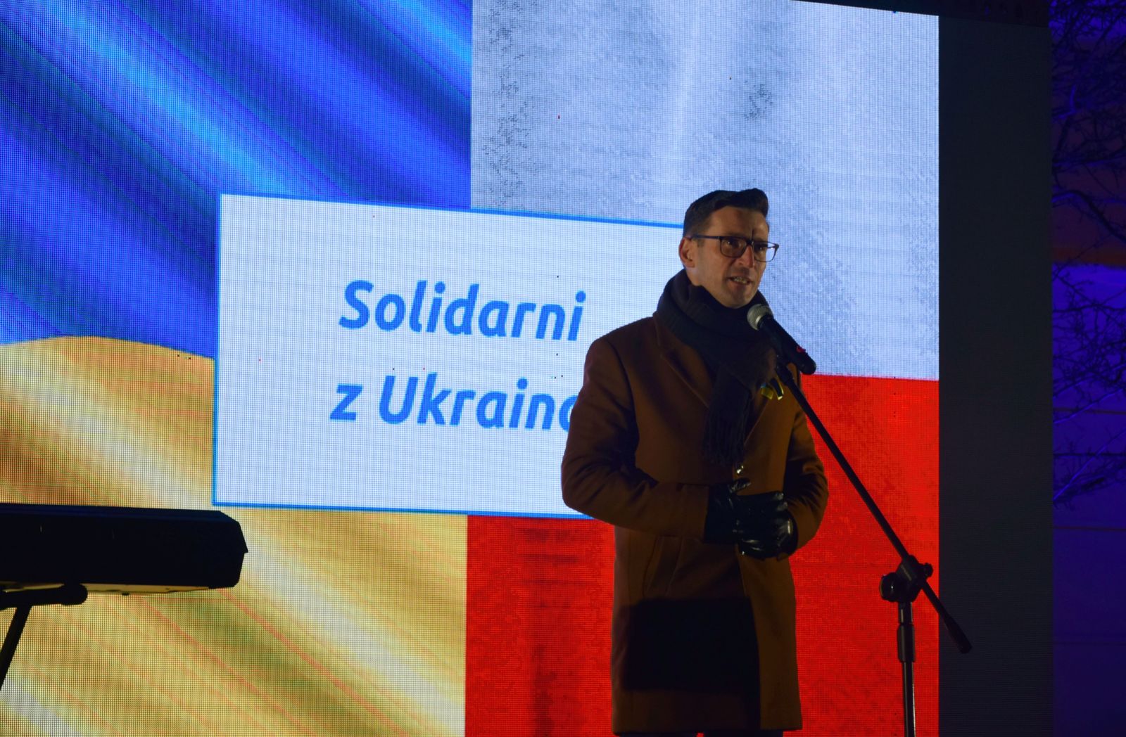 Powiększ zdjęcie. Burmistrz Dębna przemawia. W tle ukraińska i polska flaga na telebimie 