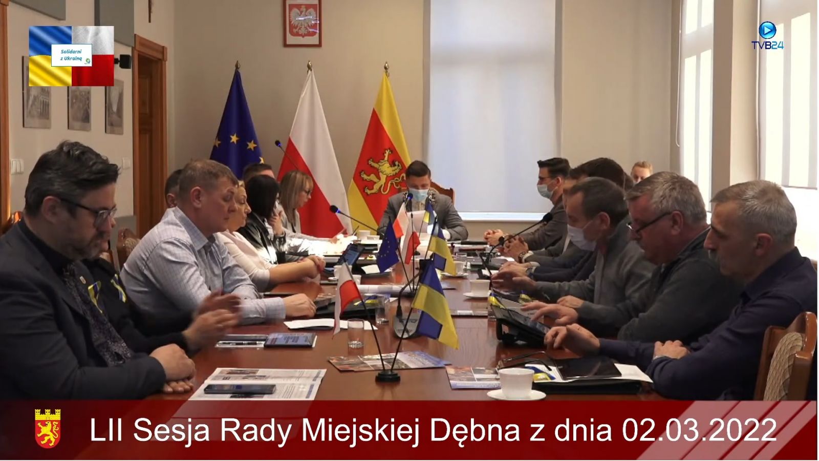 Powiększ zdjęcie. Radni siedzą przy stole, na stole stoją małe chorągiewki Ukrainy, Polski i Uni 