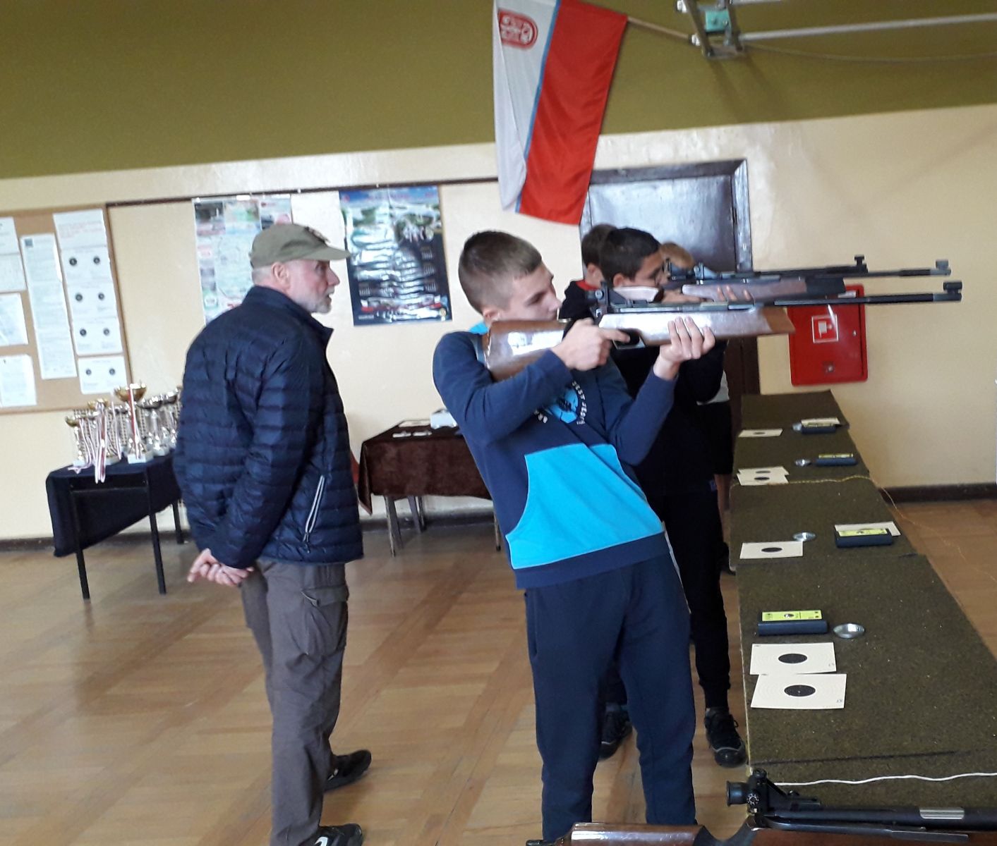 Powiększ zdjęcie. Chłopcy strzleają, z tyłu stoi mężczyzna