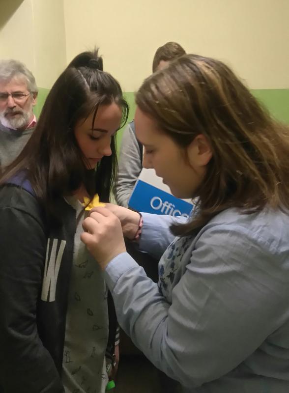 Powiększ zdjęcie. Uczennica wpina drugiej uczennicy żonkila