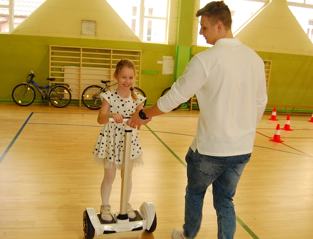Powiększ zdjęcie. Uczennica z pomocą instruktora jedzie na segway'u 