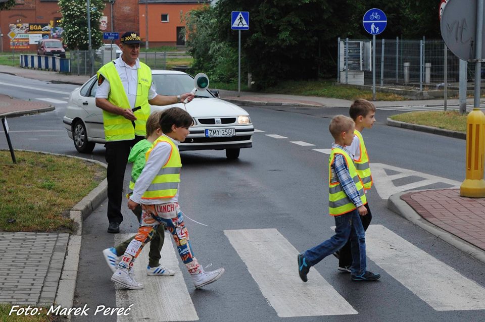 Uczniowie w asyście komandanta Straży Miejskiej przechodzą prtzez jezdnię.