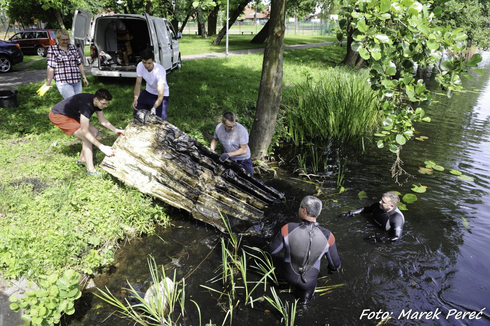 Uczestnicy akcji wyciagają śmieci z brzegu jeziora