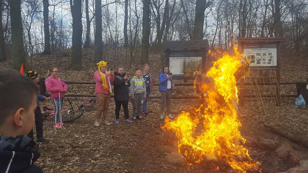 Dzieci stoją wokół paleniska, w którym pali się kukła