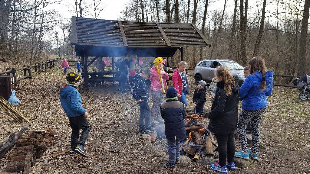 Dzieci stoją wokół paleniska i trzymają kiełbaski na patykach