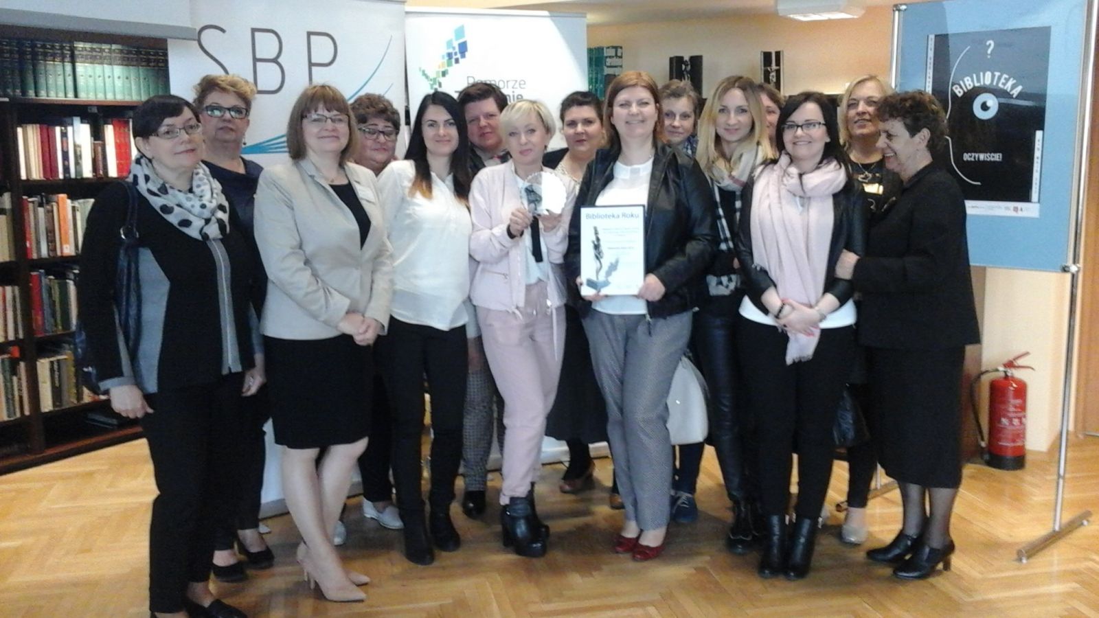 Powiększ zdjęcie. Wszyscy pracownicy biblioteki, w środku stoi dyrektor M.Piotrowska pokazuje dyplom