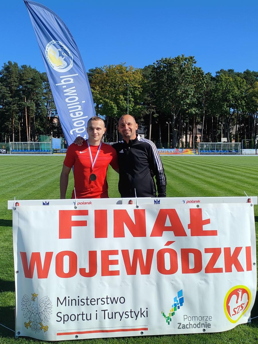 Od lewej: Karol Radziukiewicz z medalem na szyi stoi z opiekunem. Panowie objęci. Nogi zasłonięte banererem finał wojewódzki 