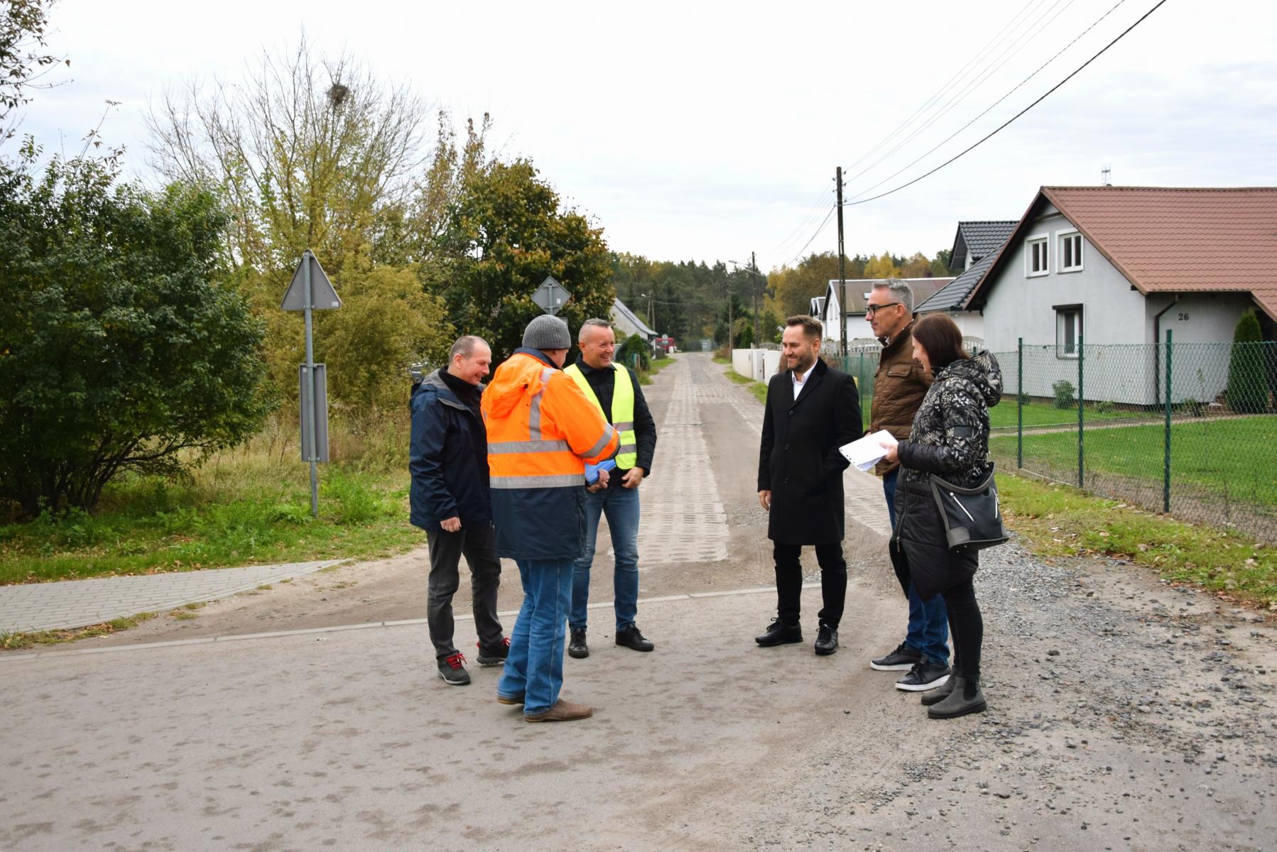 6 osób wymienionych w informacji stoi na drodze. Kobieta po prawej stronie trzyma dokumenty w ręku.