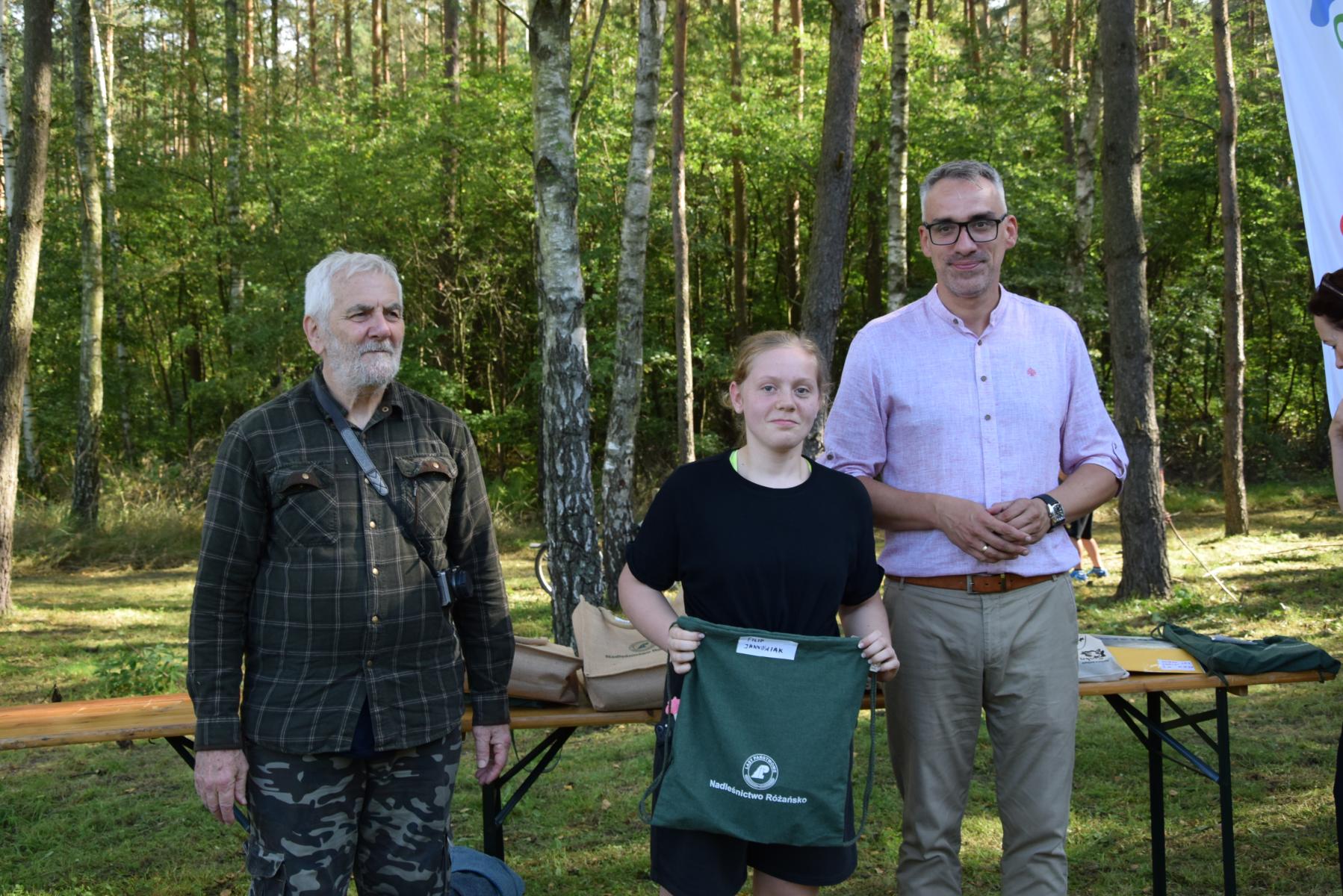 Od lewej stoją: Marek Schiller, dziewczyna z worekim zielonym w ręku, Wojciech Czepułkowski, w tle las i zieleń