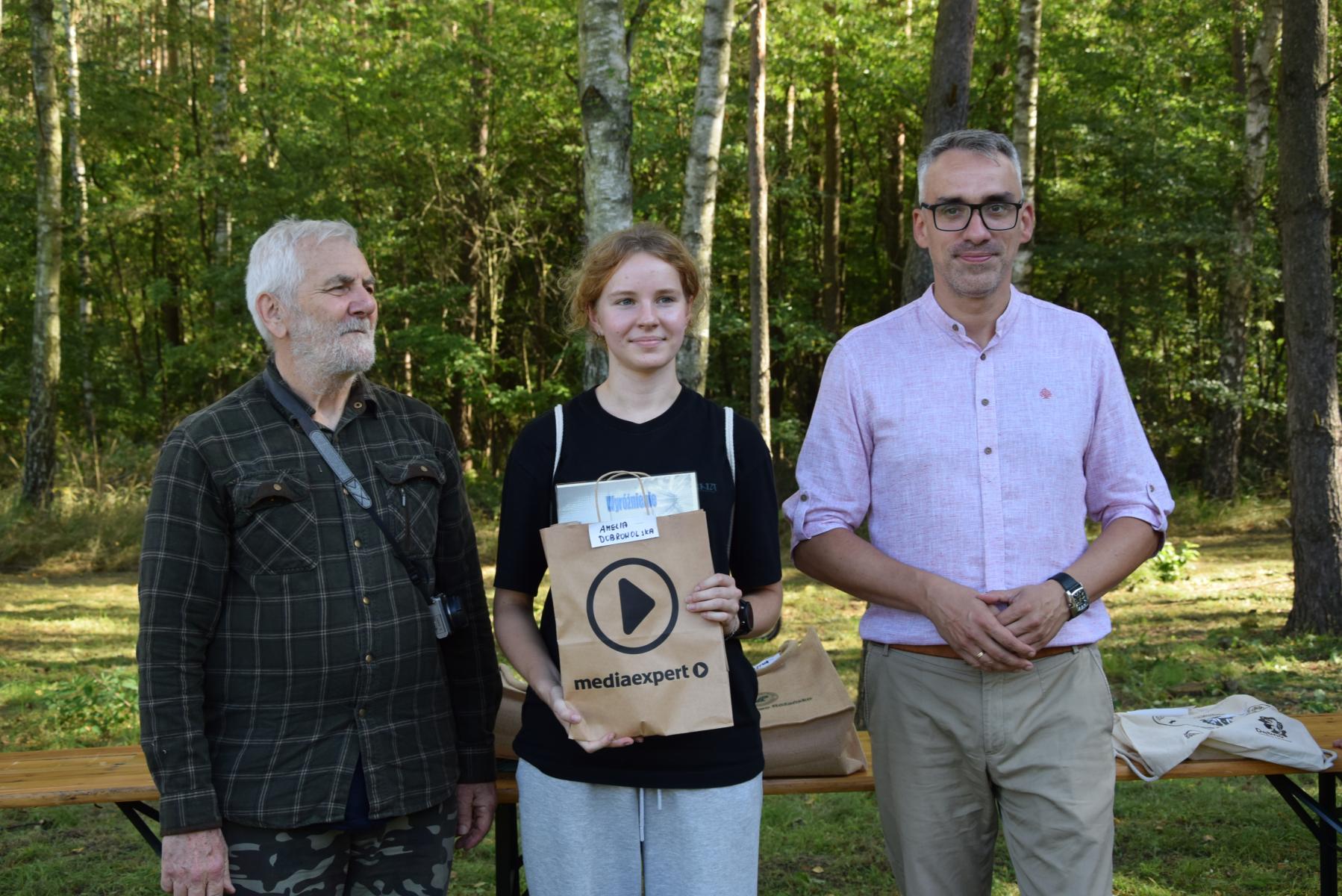 Od lewej stoją: Marek Schiller, dziewczyna z torebką w ręku, Wojciech Czepułkowski, w tle las i zieleń