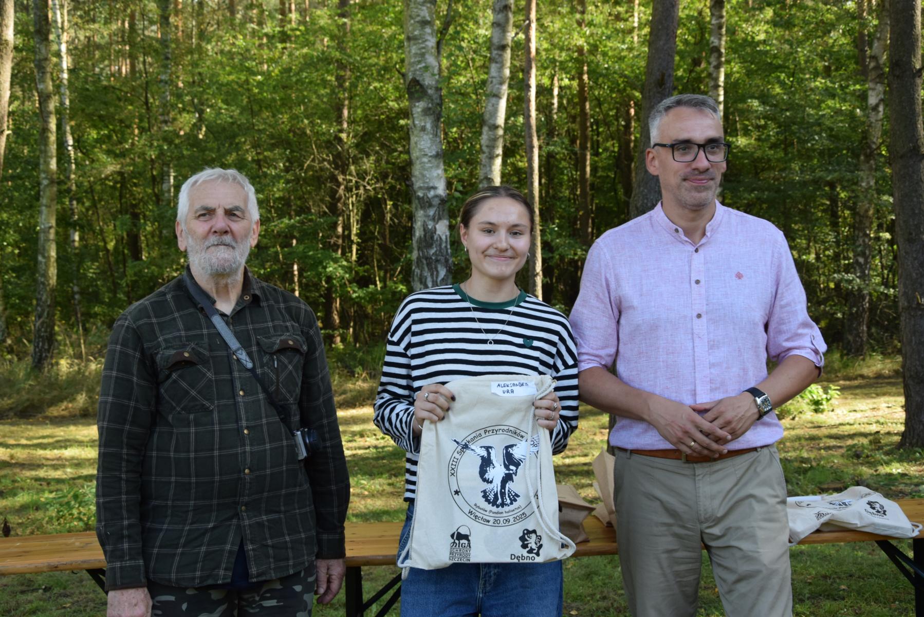 Od lewej stoją: Marek Schiller, dziewczyna z workiem w ręku, Wojciech Czepułkowski, w tle las i zieleń