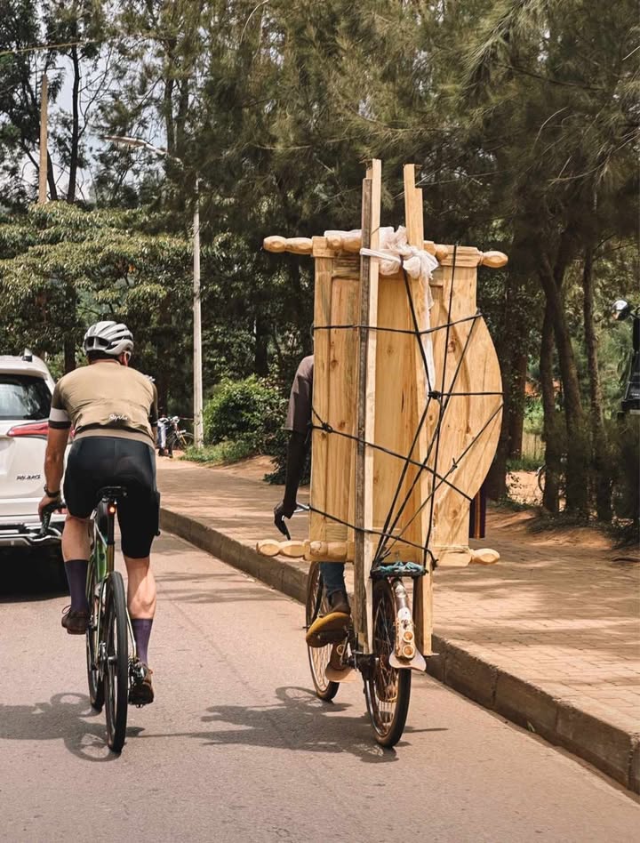 Rowerzysta jedzie ulicą, po prawej stronie rowersta na bagażniku przewozi drewniany duży pakunek.  