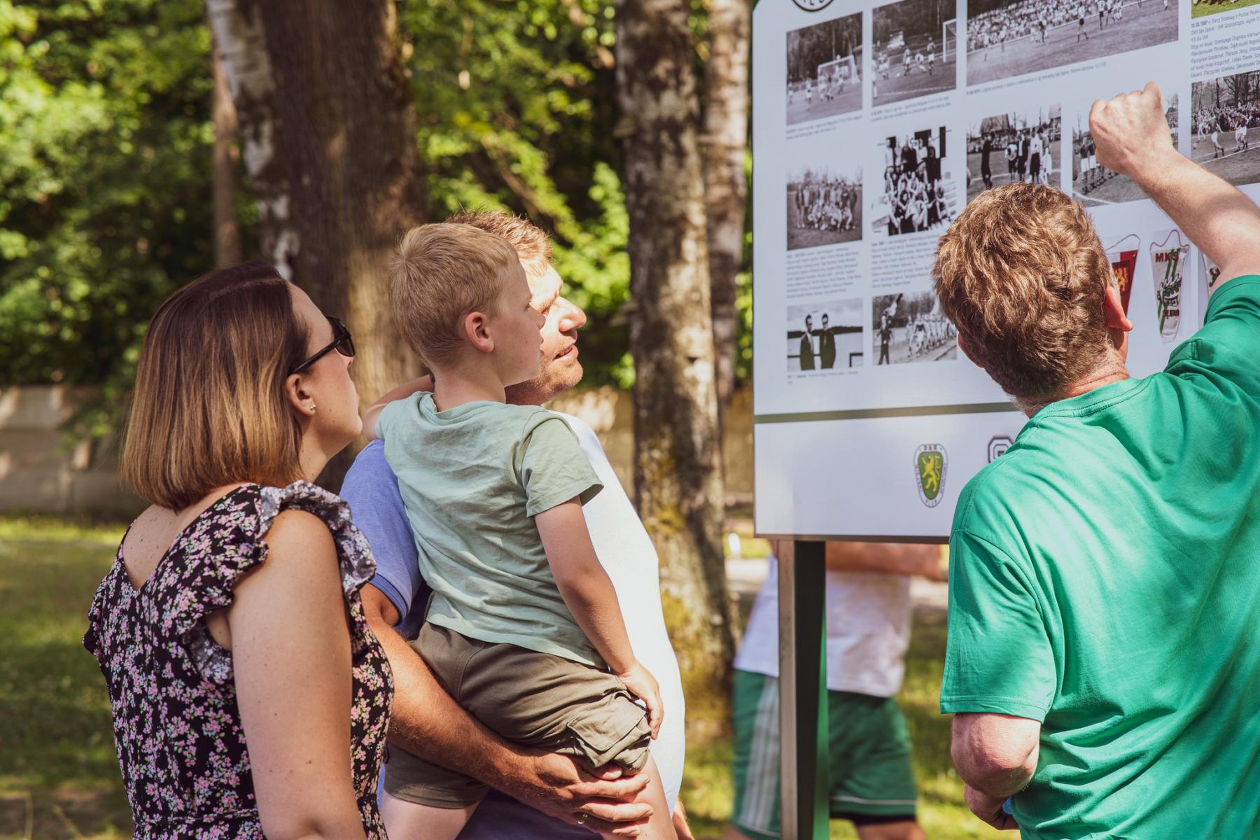 Ludzie stoja bokiem przed tablicą ze zdjęciami