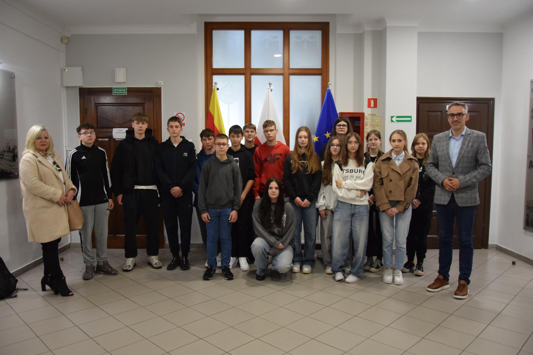 Grupa uczniwó stoi na halu, o d lewej burmistrz, od prawej nauczycielka 