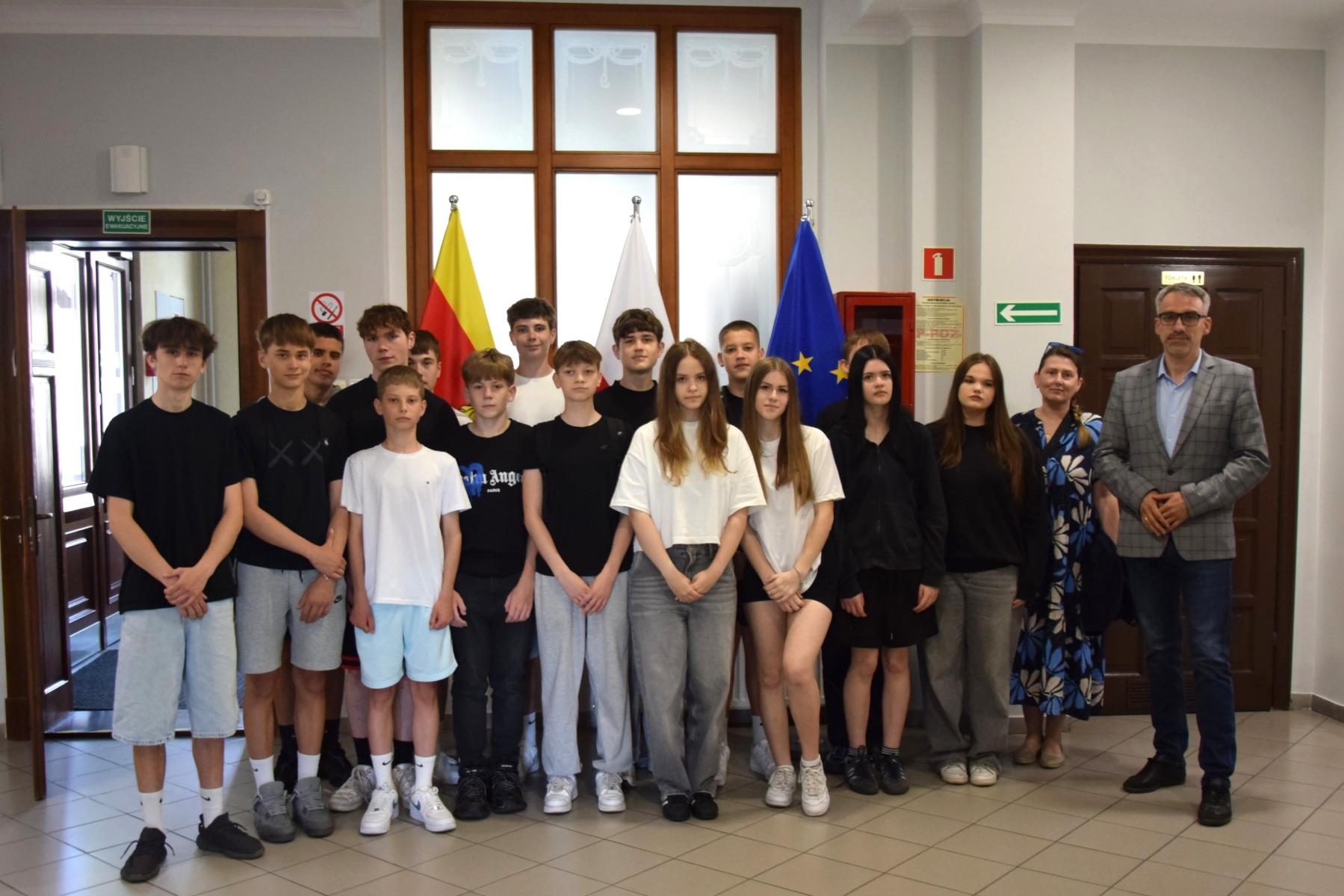 Grupa uczniów stoi na holu. od prawej burmistrz, obok nauczycielka 