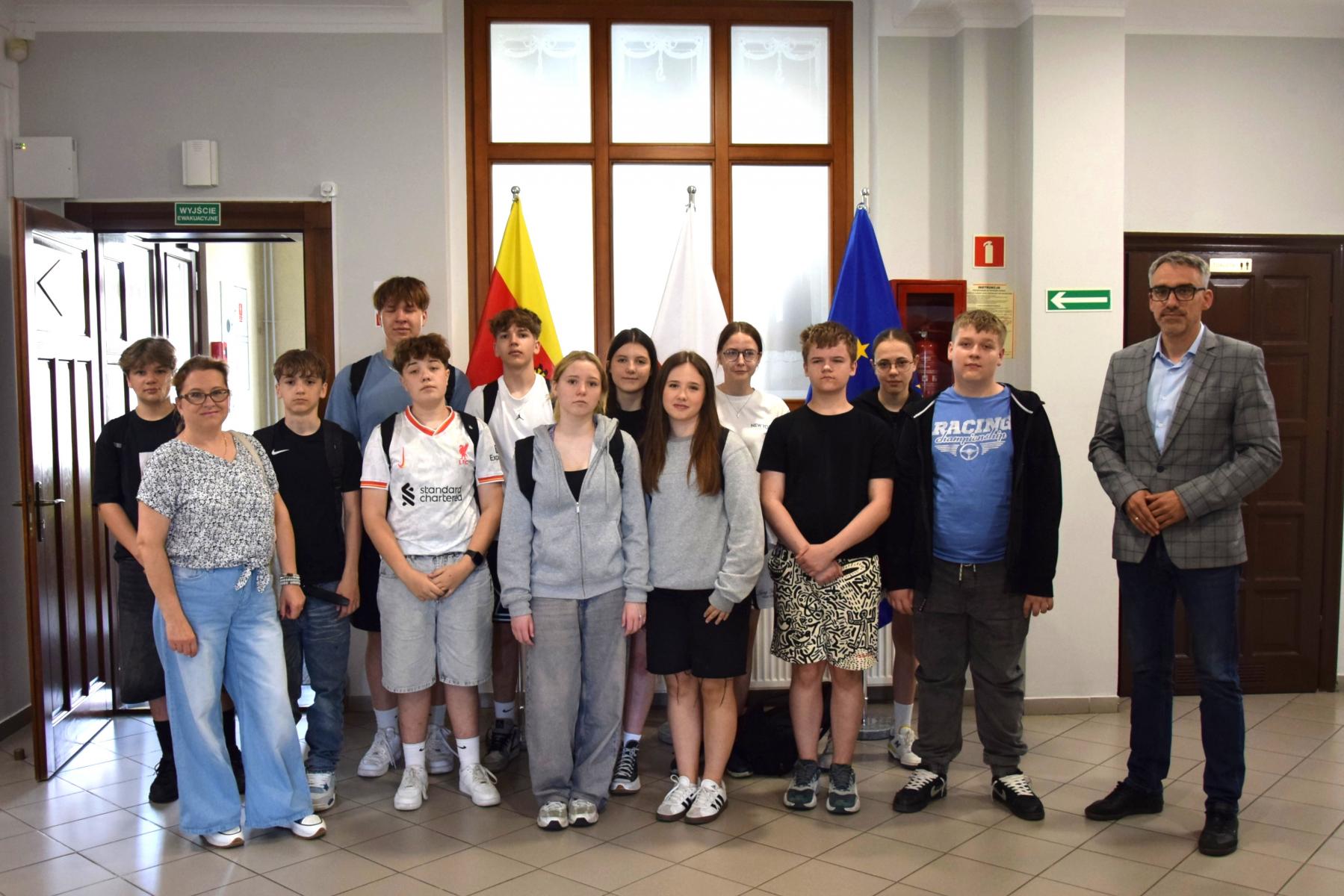 Grupa uczniwó stoi na holu, od lewej burmistrz, od prawej z przodu nauczycielka 