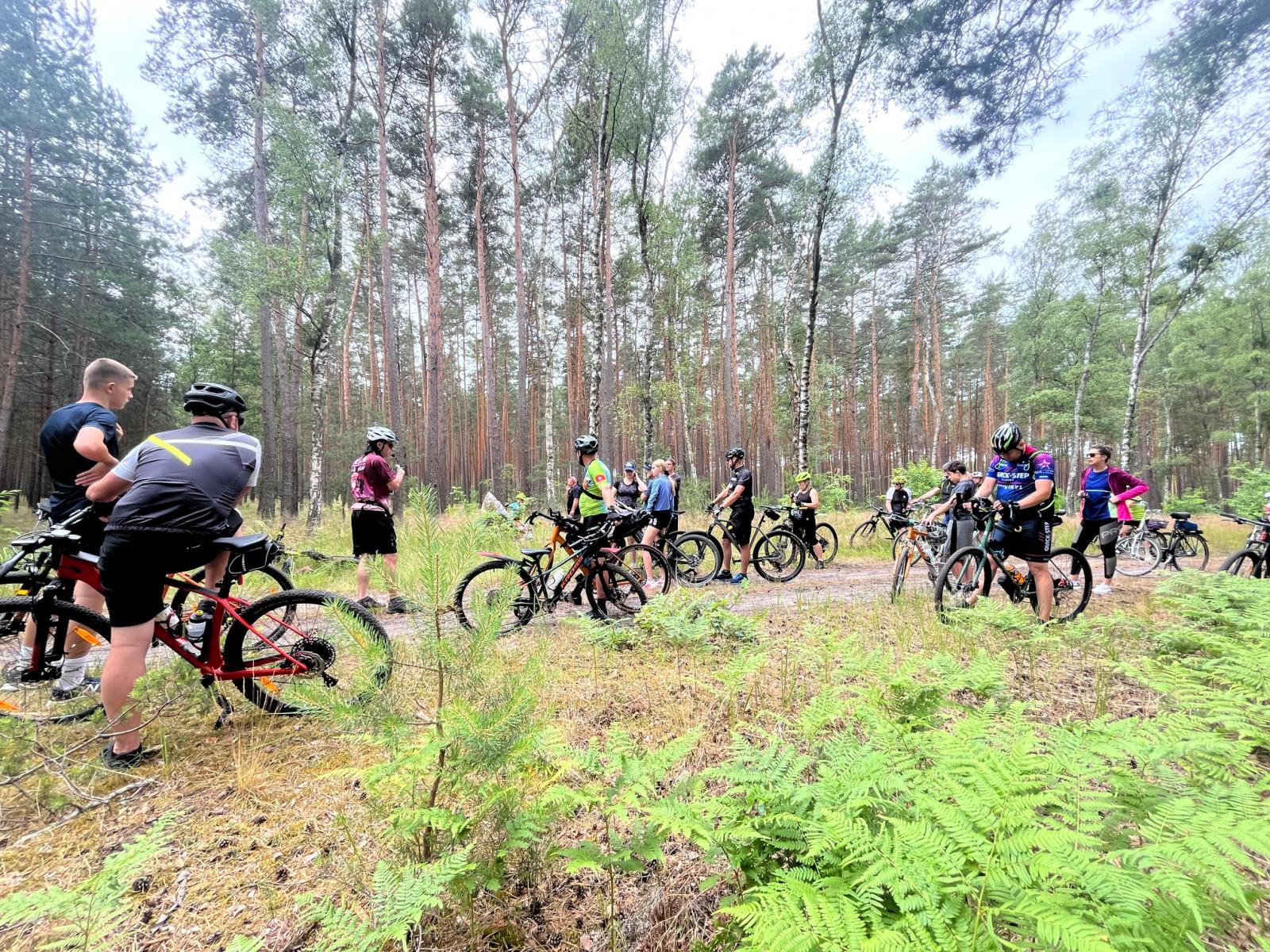 Uczestnicy stoją z rowerami w lesie, przy groobie żołnierzy rosyjskich 
