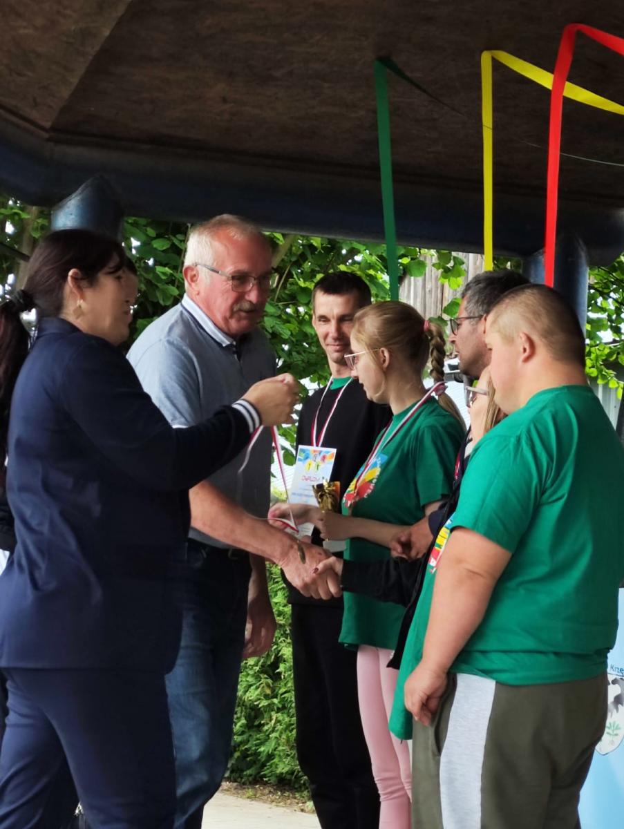 Uczestnicy stoją w rzędzie, dekoracji medalami dokonuje mężczyzna i kobieta. 