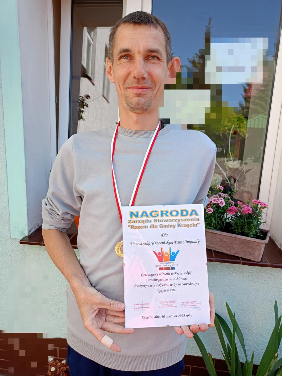 Uczestnik WTZ trzyma dyplom, medal zaiweszony na szyi 