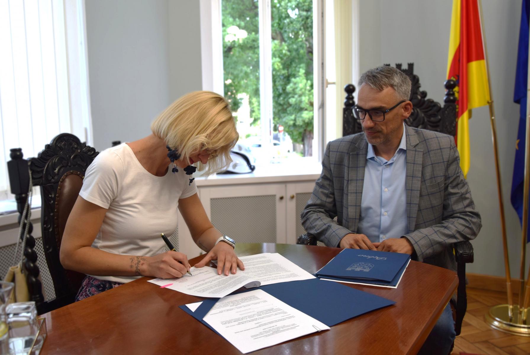 Kobieta siedzi przy stole podpisuje dokument, obok siedzi mężczyzna - burmistrz 